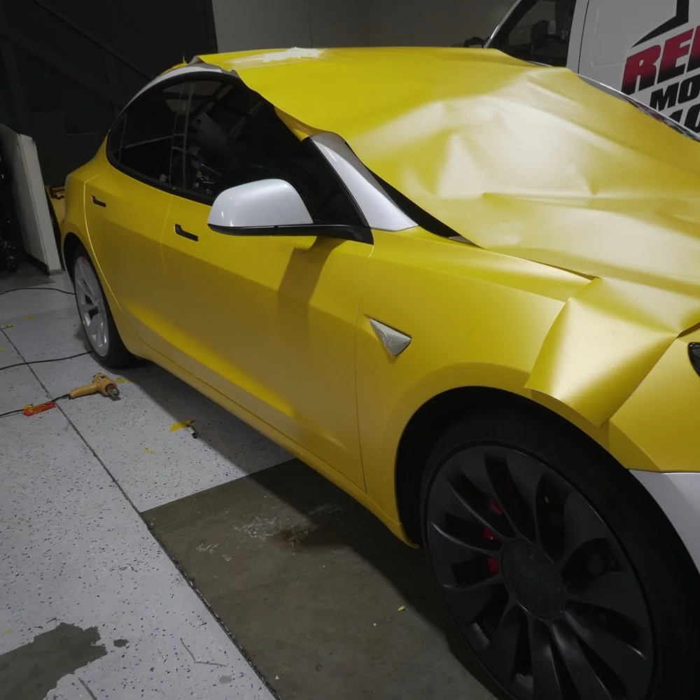 Yellow vinyl going onto a Tesla in the shop, partway through the wrap
