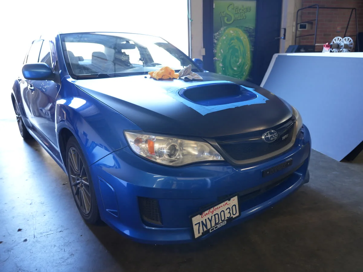 Blue Subaru WRX with a partial matte wrap in the shop bay