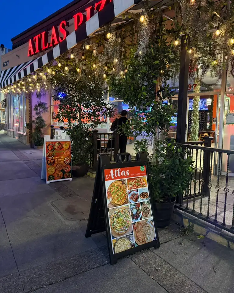 Atlas Pizza sidewalk A-frame sign outside the restaurant at dusk