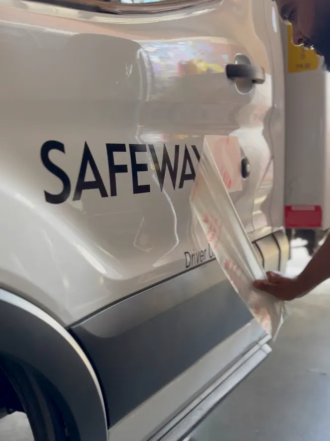 A Safeway door graphic being smoothed onto a van by hand
